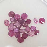 Clear close-up photo of multiple faceted ruby gemstones in pink to red hues, various shapes and sizes, showcasing natural luster and clarity.