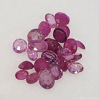 Close-up view of a collection of small faceted ruby gemstones in varying shades of red and pink.