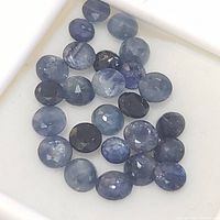Close-up photo of multiple oval faceted blue sapphire gemstones in different deep and light blue shades in a white display box.