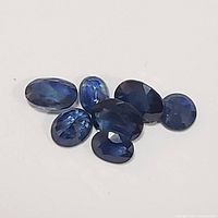 Seven deep blue faceted genuine sapphire gemstones on white background