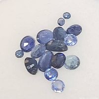Loose sapphire gemstones in various shapes and blue hues on a white background.