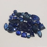 Top view of collection of various shaped genuine sapphire gemstones in multiple shades of blue on white background.