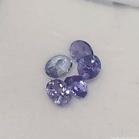 Four loose tanzanite gemstones showing different cuts and violet-blue tones on a plain surface.