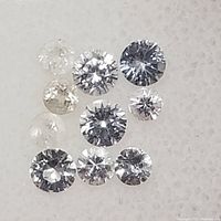 Close-up photo of multiple round cut white sapphire gemstones showing their clarity, size variation, and faceting details.