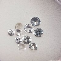 Close-up of ten loose white sapphire stones showing various sizes and round brilliant cuts on a light background.