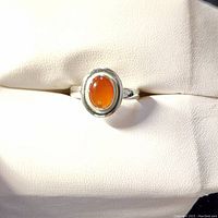 Close-up image of silver ring featuring an oval orange agate cabochon gemstone with a polished silver bezel setting on a smooth silver band.
