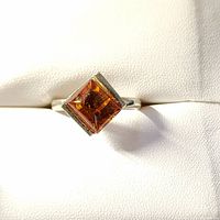 Photo showing silver ring with square amber stone, placed on white fabric background, highlighting gemstone clarity and color.