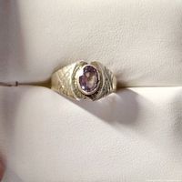 Close-up of a silver ring with an oval faceted amethyst gemstone on a beige leather ring holder.