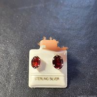 Close-up of the front view of the oval garnet earrings in sterling silver with a label stating 'STERLING SILVER'