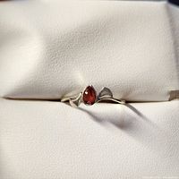 Silver ring with a pear-shaped garnet gemstone, shown on a white padded background from an angled top view.