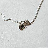 Close-up of the silver chain necklace with a small green sapphire pendant attached.