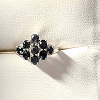 Front angled view showing the cluster setting of nine dark blue sapphire stones on a silver band.
