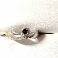 Close-up photo showing the silver ring with a small round blue sapphire stone and curved band design.
