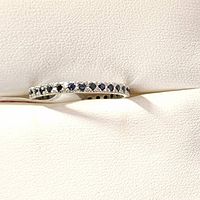 Silver ring with blue sapphire stones shown from above on white leather-like cushion, highlighting the band and stones.