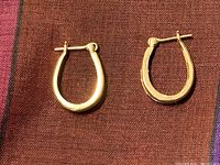 Pair of plain 10k gold oval hoop earrings shown on textile background