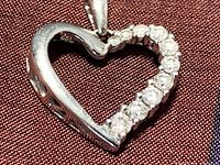 Front view of white gold heart-shaped pendant showing row of round diamonds set along one side, polished metal on the other.