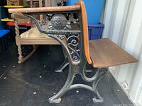 Side view of the antique school desk showing cast iron frame, wooden seat, and hinged writing surface.