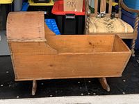 Side profile photo of antique wooden rocking crib, showing natural pine patina and curved backrest end.