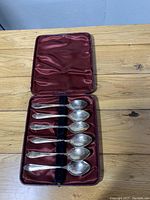 Full view of six sterling silver spoons neatly arranged in a maroon fabric-lined hinged box showing overall presentation.