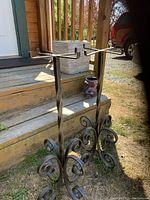 Pair of vintage wrought iron planter holders standing outdoors on grass in front of stairs. Shows twisted iron design and scrolled feet base.