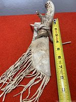 Overall view of tool sheathed in light-colored leather sheath with long fringes next to a tape measure showing approx 7 inches total length.