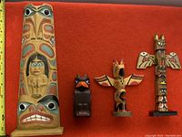 Photo showing four Indigenous style wooden carvings on a red background with measuring tape indicating the tallest totem pole is about 15 inches tall.