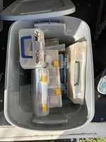 Grey plastic tote container holding several smaller plastic tackle boxes stacked inside it, showing general storage and organization of fishing gear.