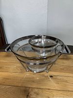 Side view of the serving set showing large and small glass bowls held inside silver-tone metal frame with black handles on each side.