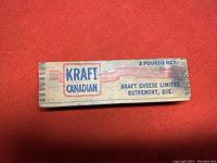 Wooden box side showing Kraft Canadian logo and 2 pounds net marking printed in blue and red on aged wood.