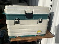 Closed green and white vintage Plano tackle box with latches on front and handles on sides.