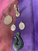 Overview photo showing all spiritual symbol items on a multicolor cloth; includes pendants, small figurine, and greenstone pendant.