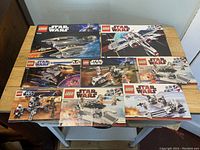 Photo showing a lot of nine LEGO Star Wars instruction manuals placed on a table, with detailed colorful covers of Star Wars spacecraft and LEGO branding.