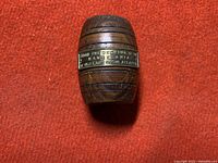 Front view of small barrel-shaped turned wood toothpick holder with brass plaque inscription from Mauretania deck wood