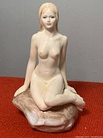 Front and side view of the nude female bone china figurine seated on a textured base