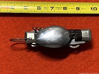 Metallic vintage multi-tool closed, with spoon cover and corkscrew visible, approximately 5.5 inches long as measured by tape.