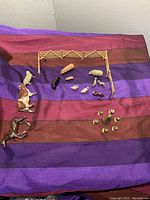 Overview showing all farm animal figures, scattered wooden fence parts, and brass miniature serving items arranged on purple and brown cloth.