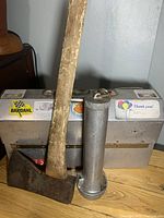 Photo of axe, flashlight, and lunch box on wooden surface against wall, showing state of wear and stickers on lunch box.