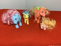 Four vintage My Little Pony figures placed together on red fabric surface with visible wear and tangled hair