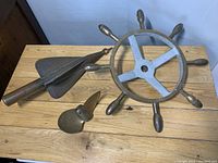 Top view of three nautical items on wooden table showing ship wheel, torpedo, and propeller.