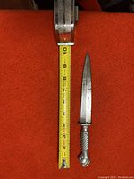Full view of vintage German dagger on red background with measuring tape showing approx. 10 inches in length.