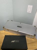 Closed silver aluminum case labeled Williams Sonoma, placed next to a black box labeled Native Essence, showing storage means for BBQ and salad sets