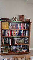 Front view of solid wood four tier bookshelf loaded with various books and decorative items on top surface.