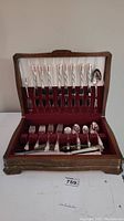 Wooden flatware canteen open showing Tudor Plate Oneida Community flatware set with knives, forks, tablespoons, teaspoons (partially missing), and dessert forks (partially missing) inside.