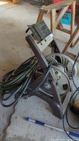 Garden hose coiled on a dark brown portable hose reel with wheels on a concrete floor near a wooden step ladder.