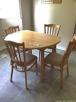 Full view of drop leaf table with four matching wooden chairs with upholstered seats on tiled floor by window in kitchen.