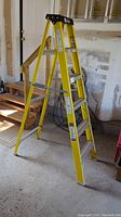 Yellow Davidson Type I A-frame ladder standing upright in garage, showing side view including steps, safety labels, and black top cap.