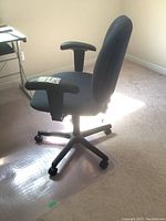 Side view of upholstered office chair showing padded armrests, fabric seat and back, and five caster legs on black plastic base.