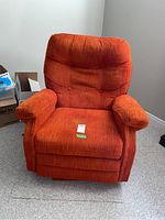 Front view of a deep orange recliner chair with padded armrests and tufted backrest, showing overall condition and style.