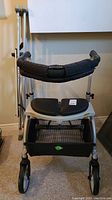 Front view of Evolution Xpresso Lite rollator with padded seat, backrest, mesh basket and two crutches leaning behind