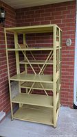 Front view of one metal shelving unit showing five adjustable shelves with attached wood stabilizers, riveted metal frame, and cross braces at the back.